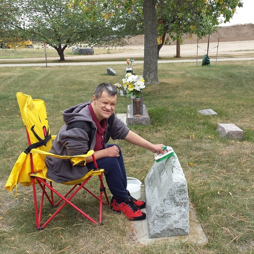 Aspire male client volunteering by scrubbing and cleaning headstones